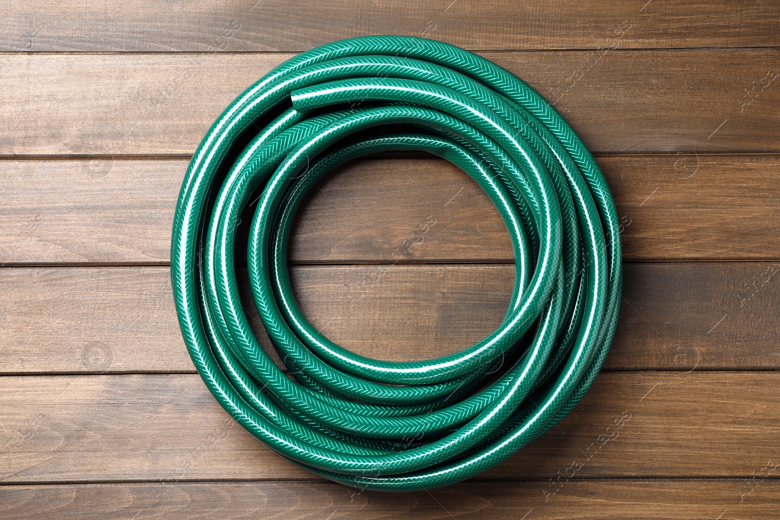 Photo of Green garden hose on wooden table, top view