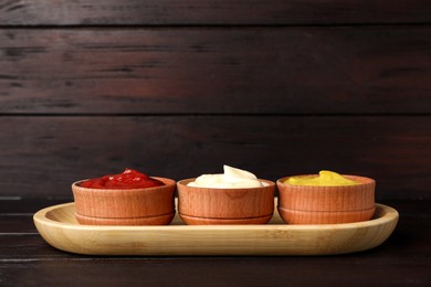 Ketchup, mayonnaise and mustard in bowls on wooden table, space for text