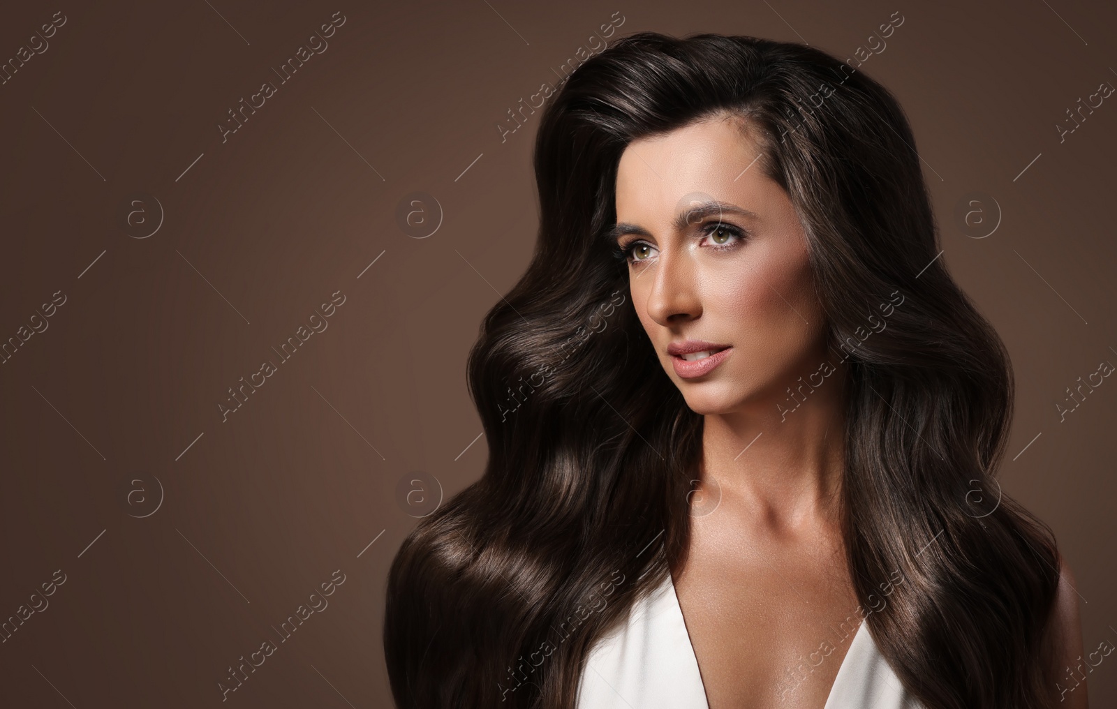 Image of Gorgeous woman with shiny wavy hair on brown background, space for text. Professional hairstyling