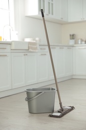 Photo of Mop and plastic bucket in kitchen. Cleaning supplies