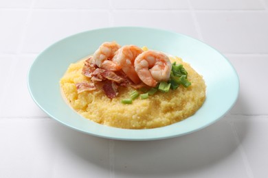 Plate with fresh tasty shrimps, bacon, grits and green onion on white tiled table