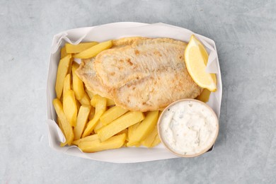 Photo of Delicious fish and chips with tasty sauce in paper box on gray table, top view
