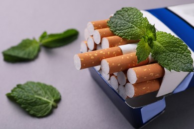 Photo of Pack of menthol cigarettes and mint leaves on grey background, closeup