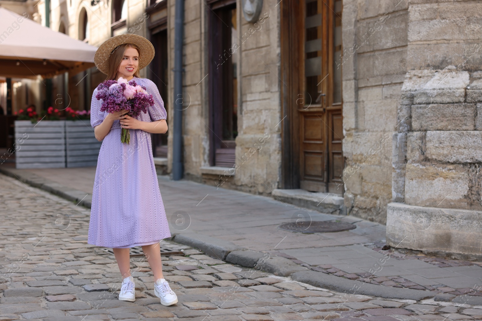 Photo of Beautiful woman with bouquet of spring flowers on city street, space for text