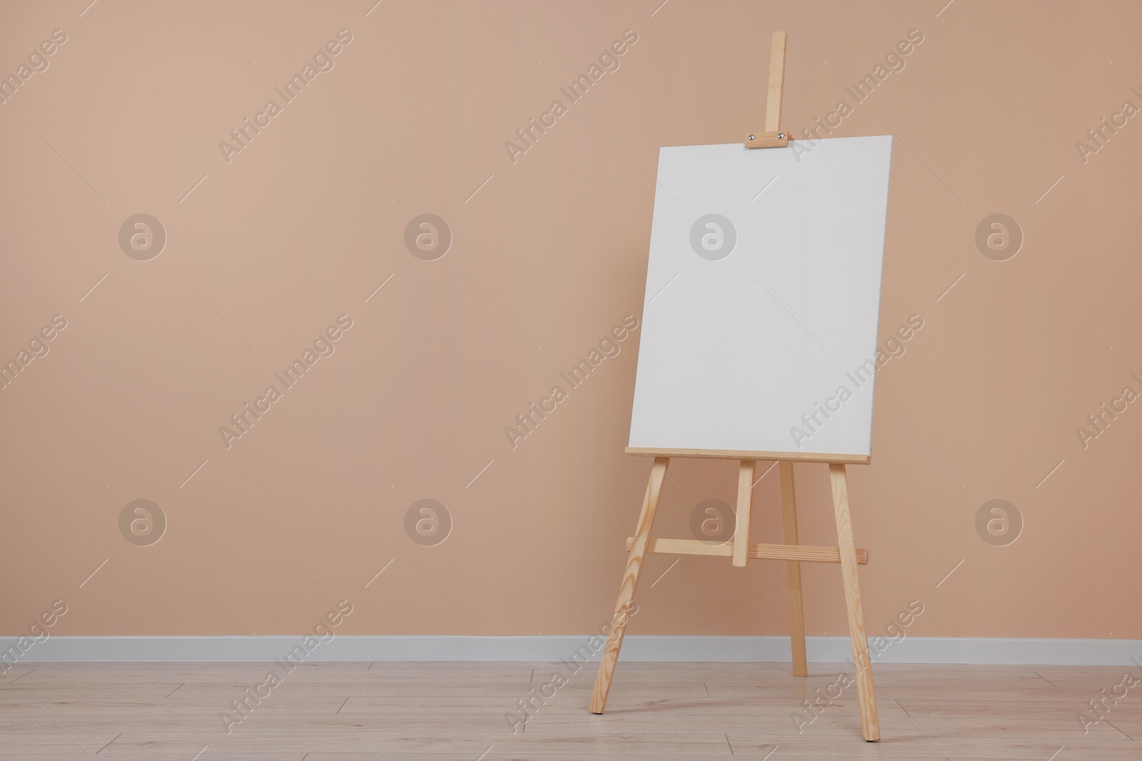 Photo of Wooden easel with blank canvas near beige wall indoors. Space for text