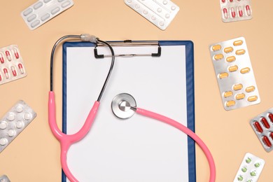 Stethoscope and clipboard surrounded by pills on beige background, flat lay. Medical tool