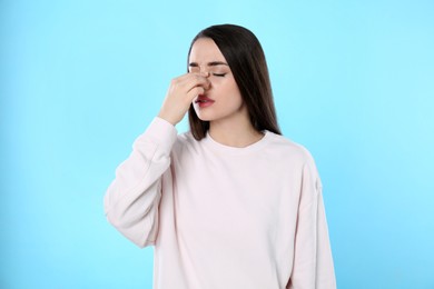 Photo of Young woman suffering from runny nose on light blue background