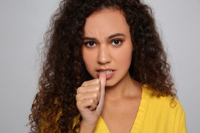 African-American woman biting her nails on grey background