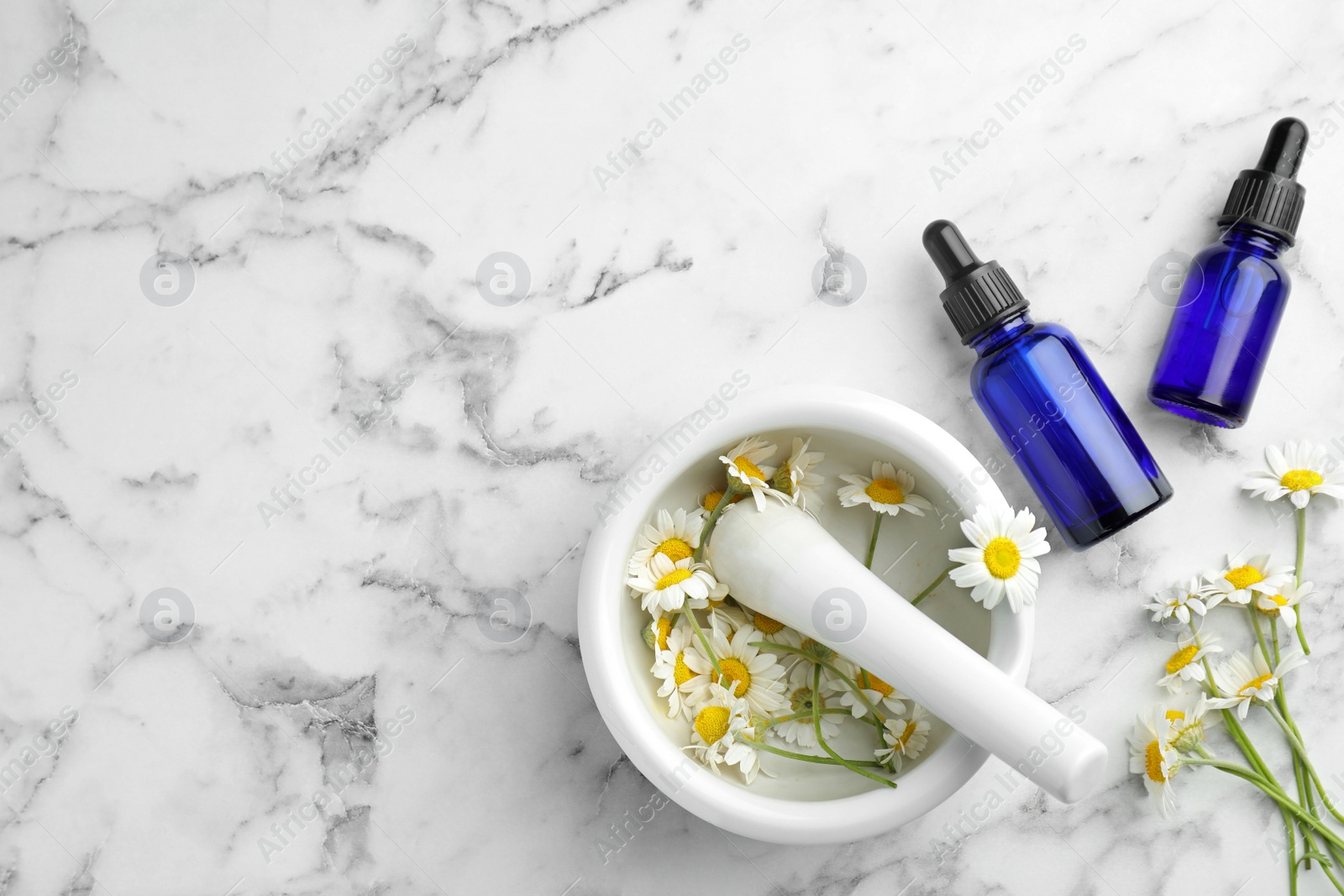 Photo of Flat lay composition with bottles of chamomile essential oil and flowers on marble table. Space for text