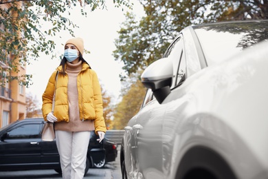 Photo of Young woman in medical face mask and gloves walking outdoors. Personal protection during COVID-19 pandemic