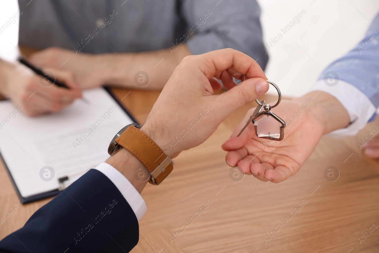 Photo of Real estate agent giving key with trinket to client in office, closeup