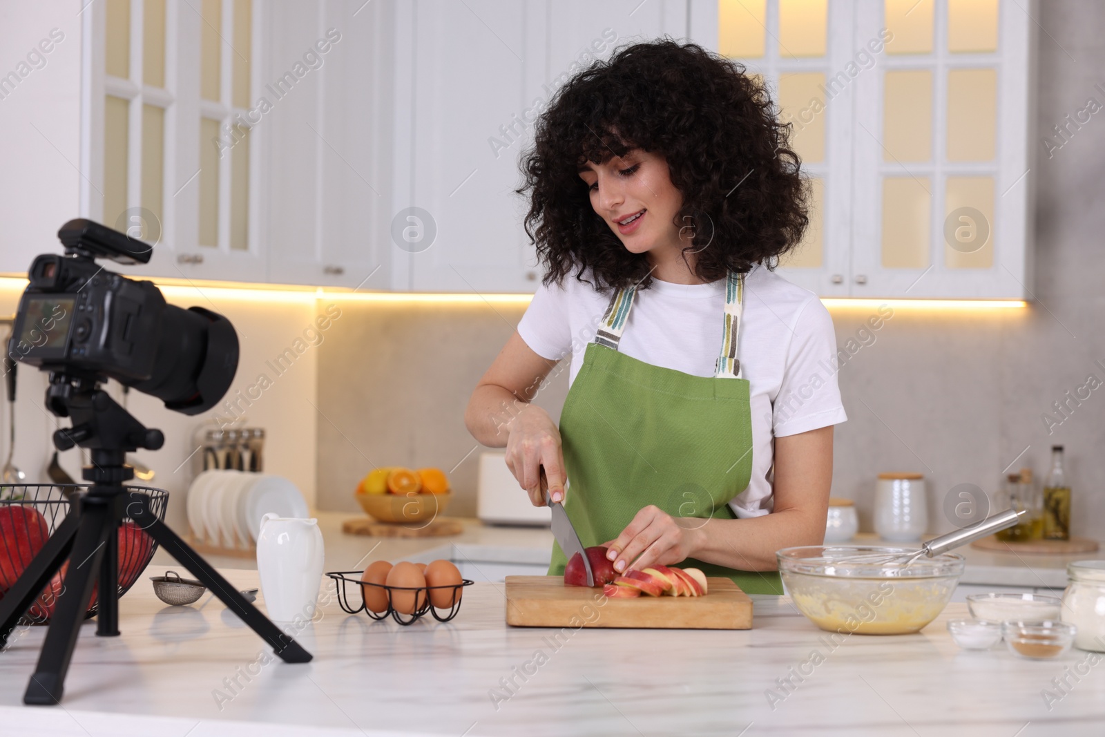 Photo of Smiling food blogger cooking while recording video in kitchen