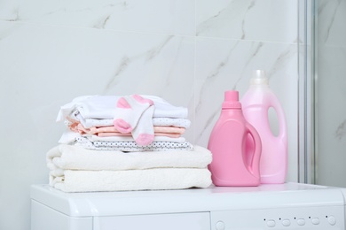 Photo of Bottles of detergent and children's clothes on washing machine in bathroom