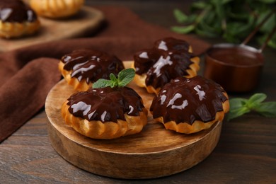 Delicious profiteroles with chocolate spread and mint on wooden table, closeup