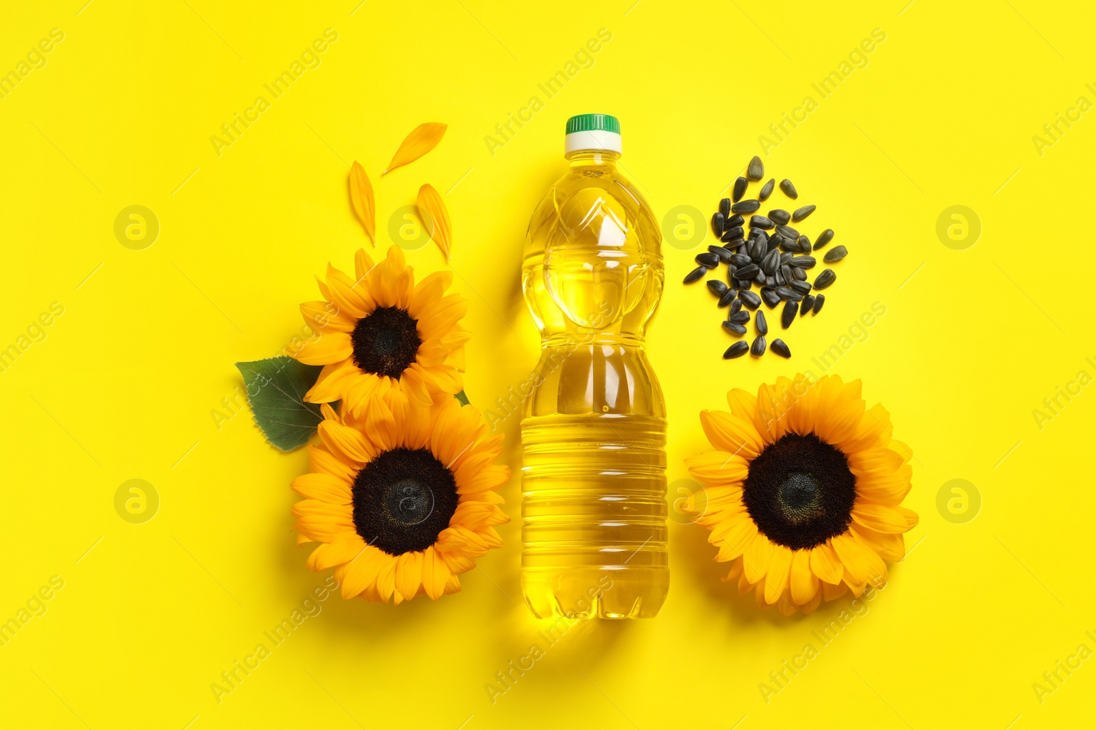 Photo of Bottle of cooking oil, sunflowers and seeds on yellow background, flat lay