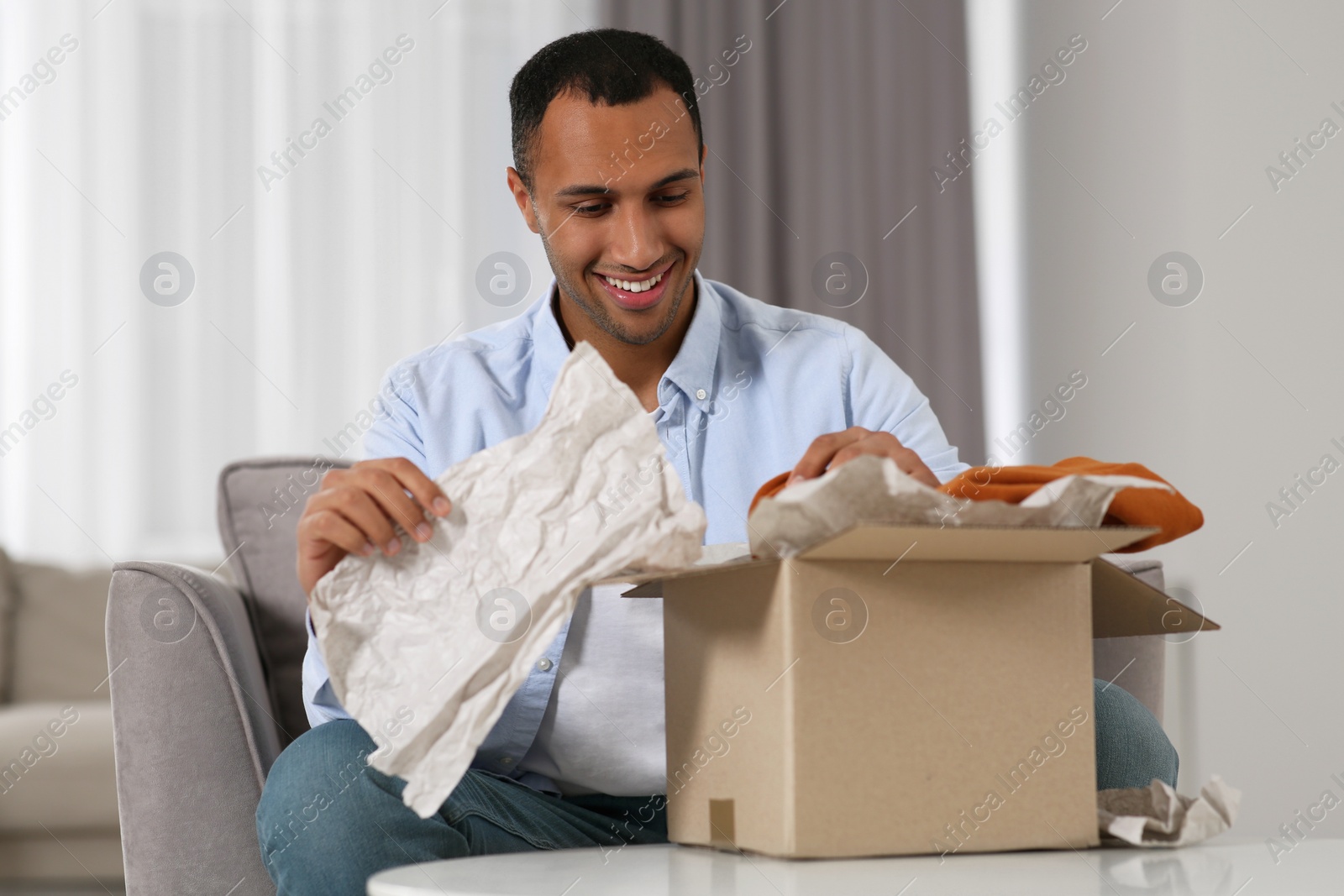 Photo of Happy young man opening parcel at home. Internet shopping