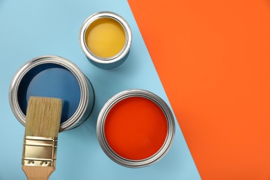 Cans of different paints and brush on color background, flat lay. Space for text