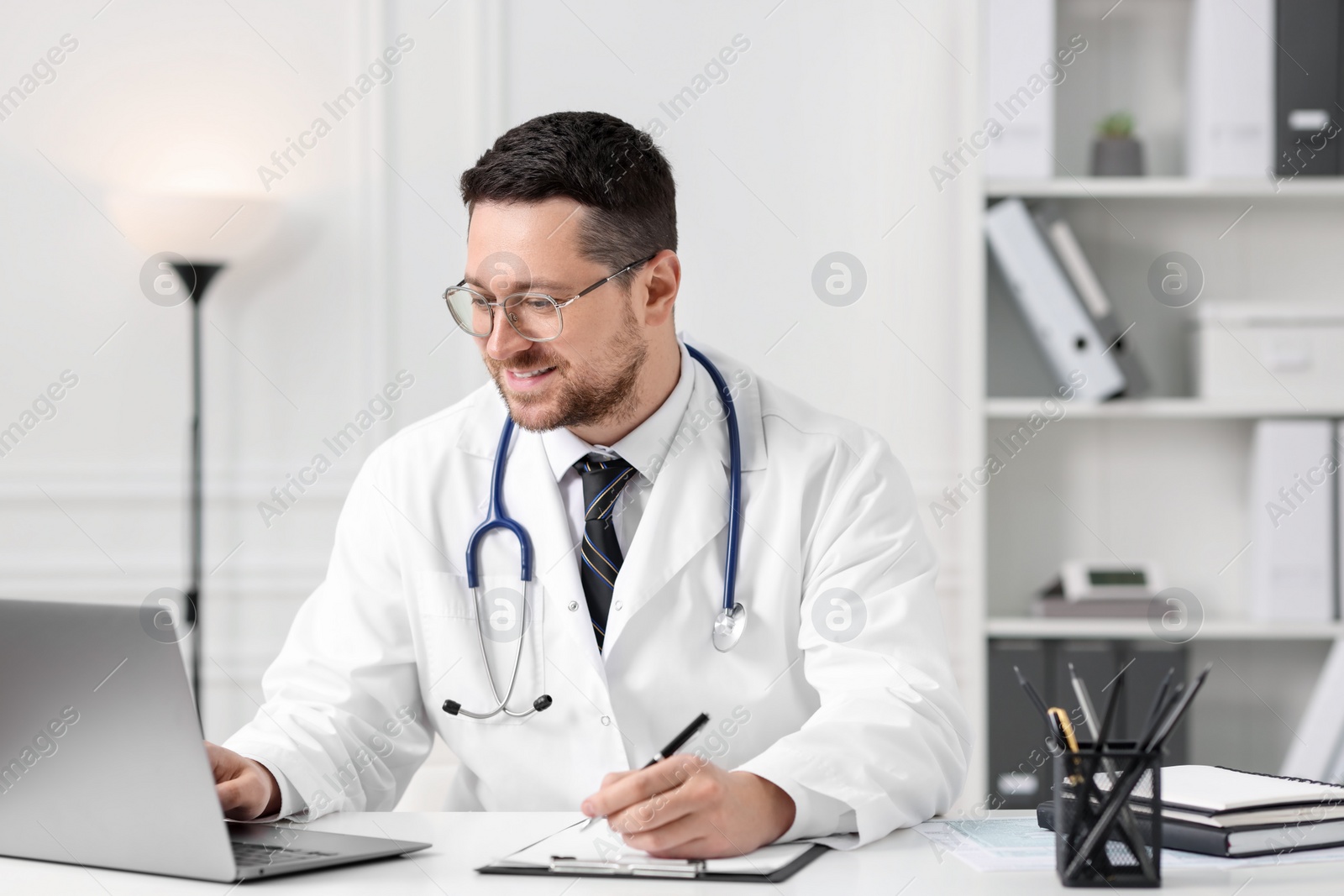 Photo of Doctor having online consultation via laptop at table in clinic