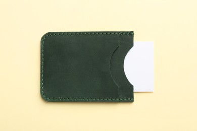 Leather business card holder with blank card on beige background, top view