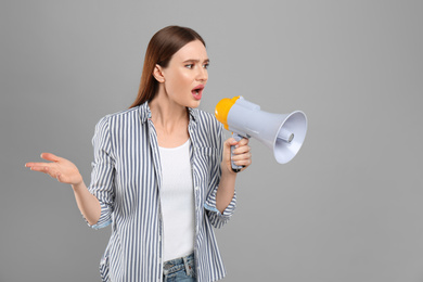 Photo of Emotional young woman with megaphone on light grey background