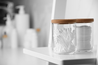 Photo of Glass jars with cotton pads and swabs on white shelf in bathroom, closeup. Space for text