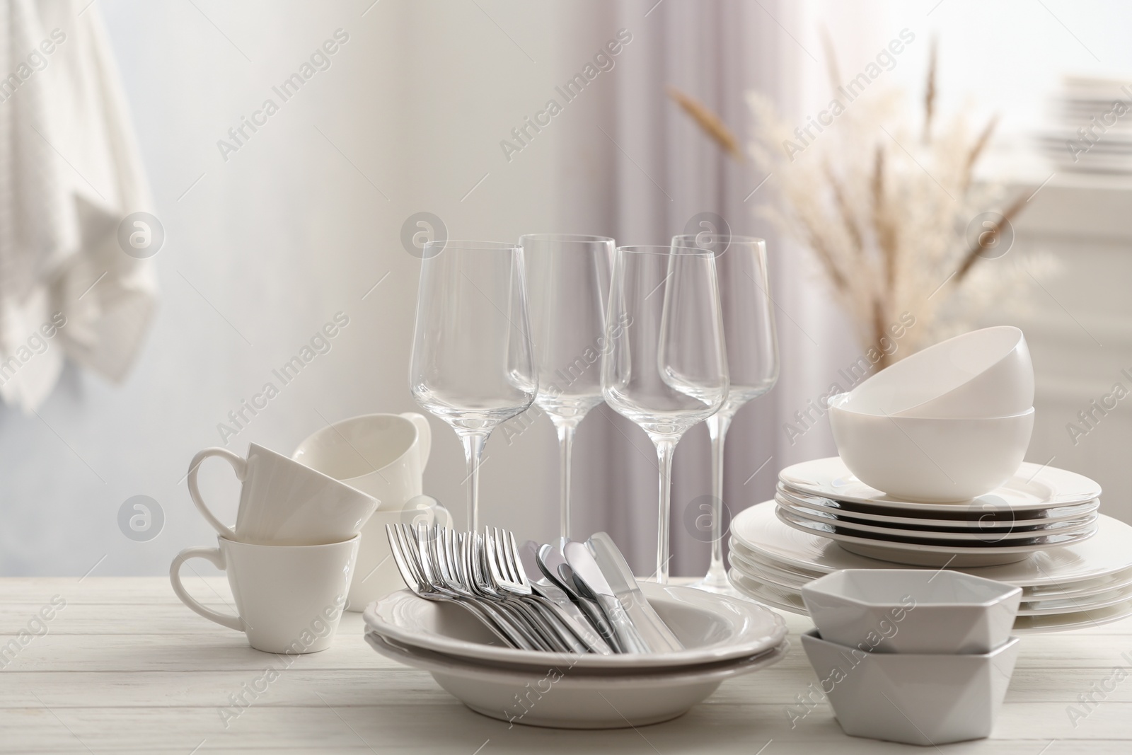 Photo of Set of clean dishware, cutlery and wineglasses on white table indoors
