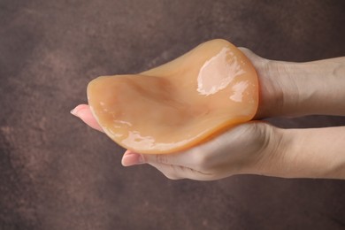 Photo of Making kombucha. Woman holding Scoby fungus on brown background, closeup
