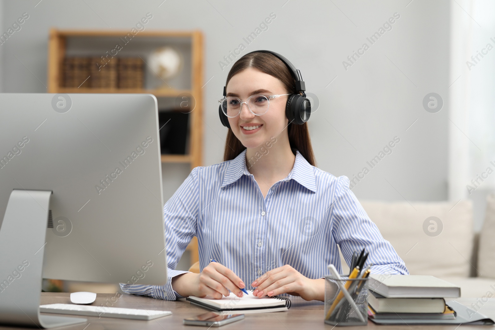 Photo of E-learning. Young woman taking notes during online lesson at table indoors