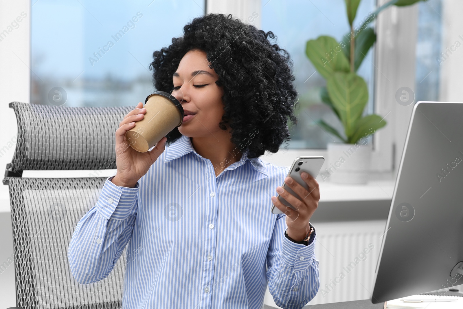 Photo of Young woman drinking coffee while working on computer in office