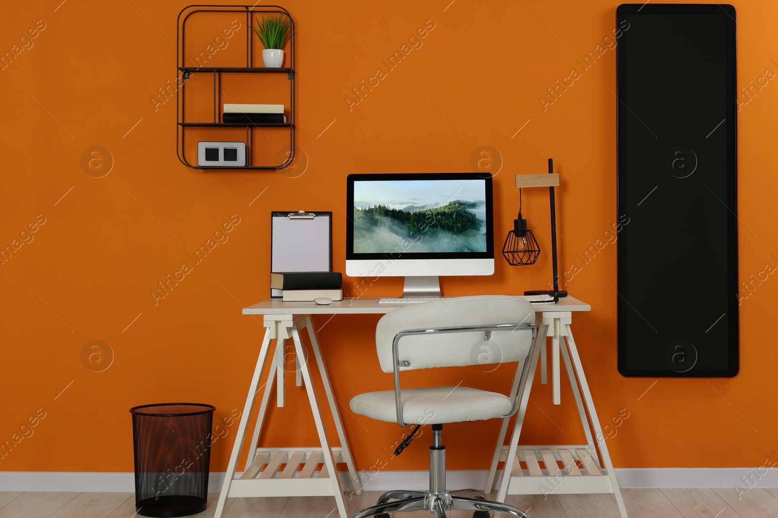 Photo of Workplace with modern computer on wooden desk and comfortable chair near orange wall. Home office