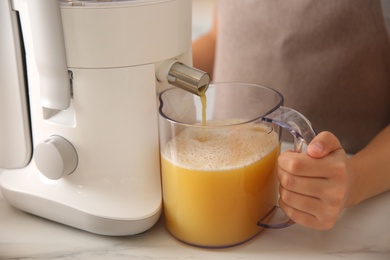 Young woman making tasty fresh juice at table in kitchen, closeup