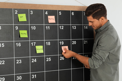 Photo of Handsome man putting sticky note on board calendar