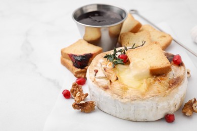 Photo of Tasty baked camembert with crouton, thyme, walnuts and pomegranate seeds on white marble table, closeup. Space for text