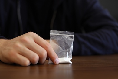 Criminal holding drug at wooden table, closeup