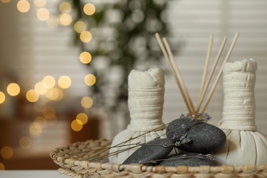 Photo of Spa composition. Herbal bags, stones, reed diffuser and dry lavender flowers in wicker tray indoors, bokeh effect