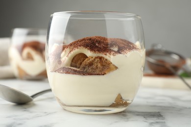 Photo of Delicious tiramisu in glass and spoon on white marble table, closeup