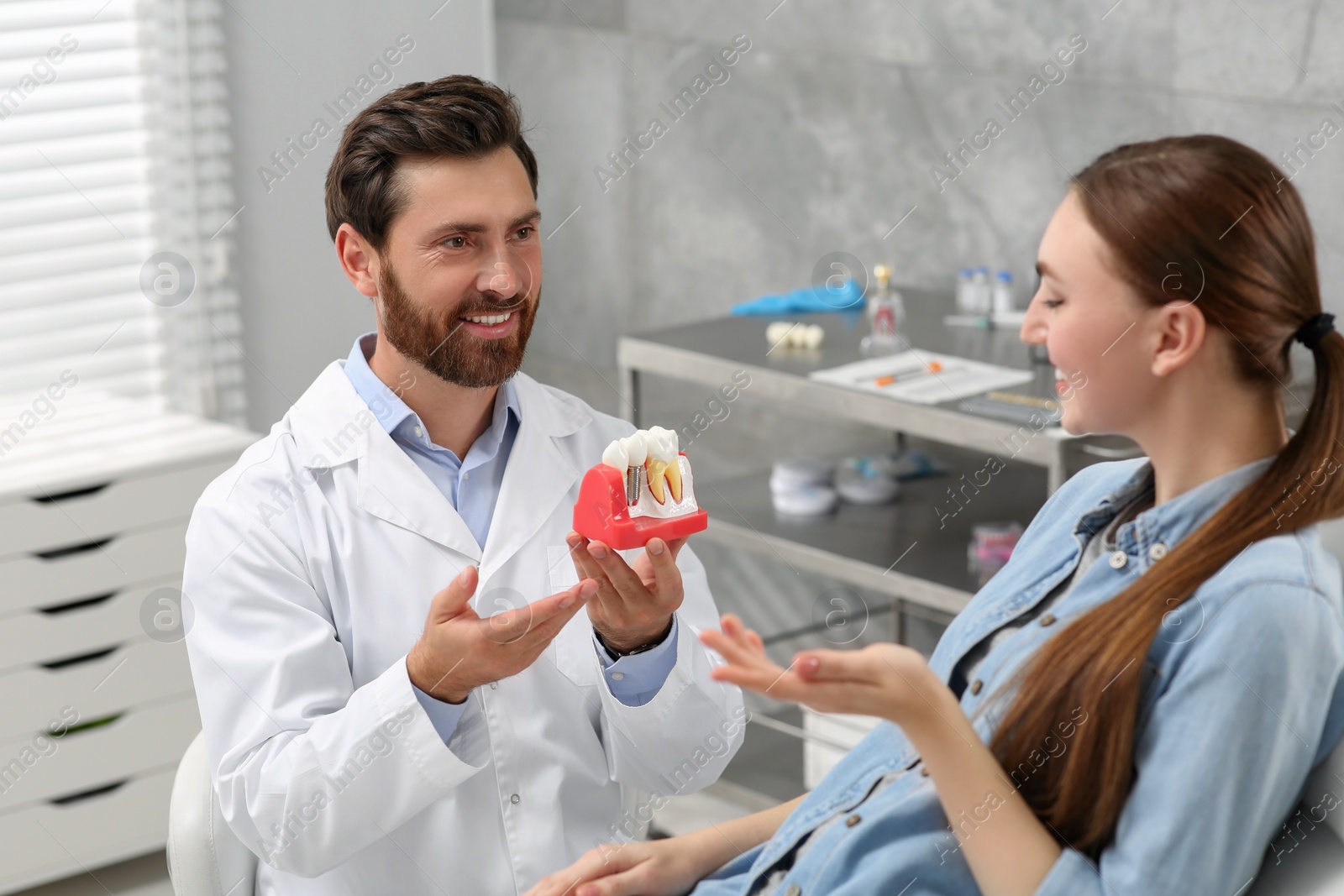 Photo of Doctor with educational model of dental implant consulting patient in clinic