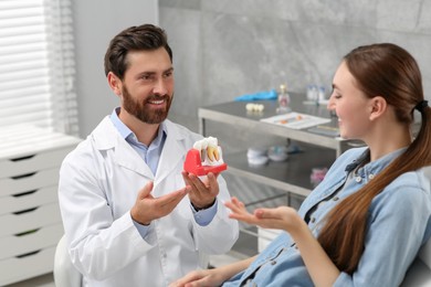 Photo of Doctor with educational model of dental implant consulting patient in clinic