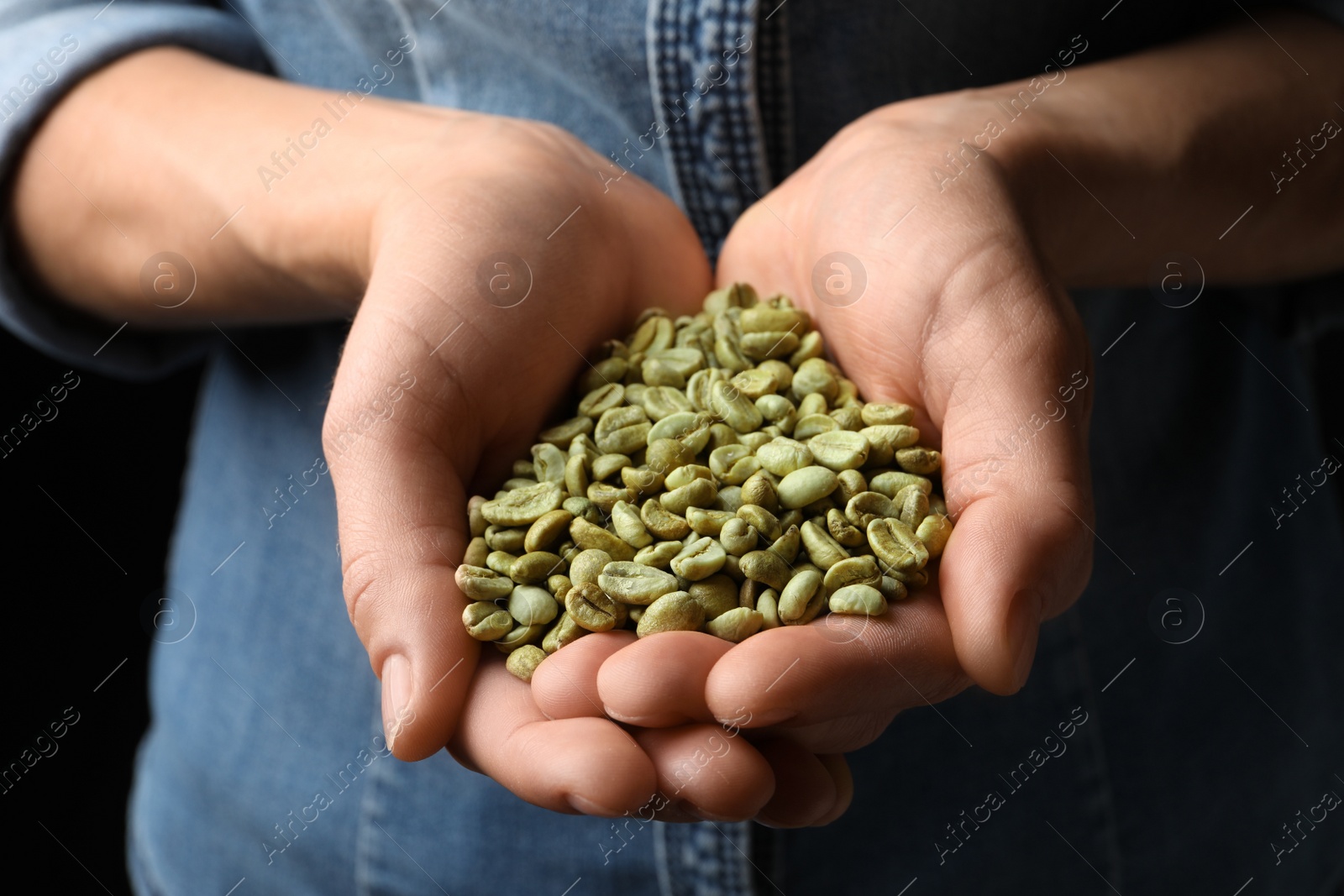Photo of Woman holding pile of green coffee beans on black background, closeup