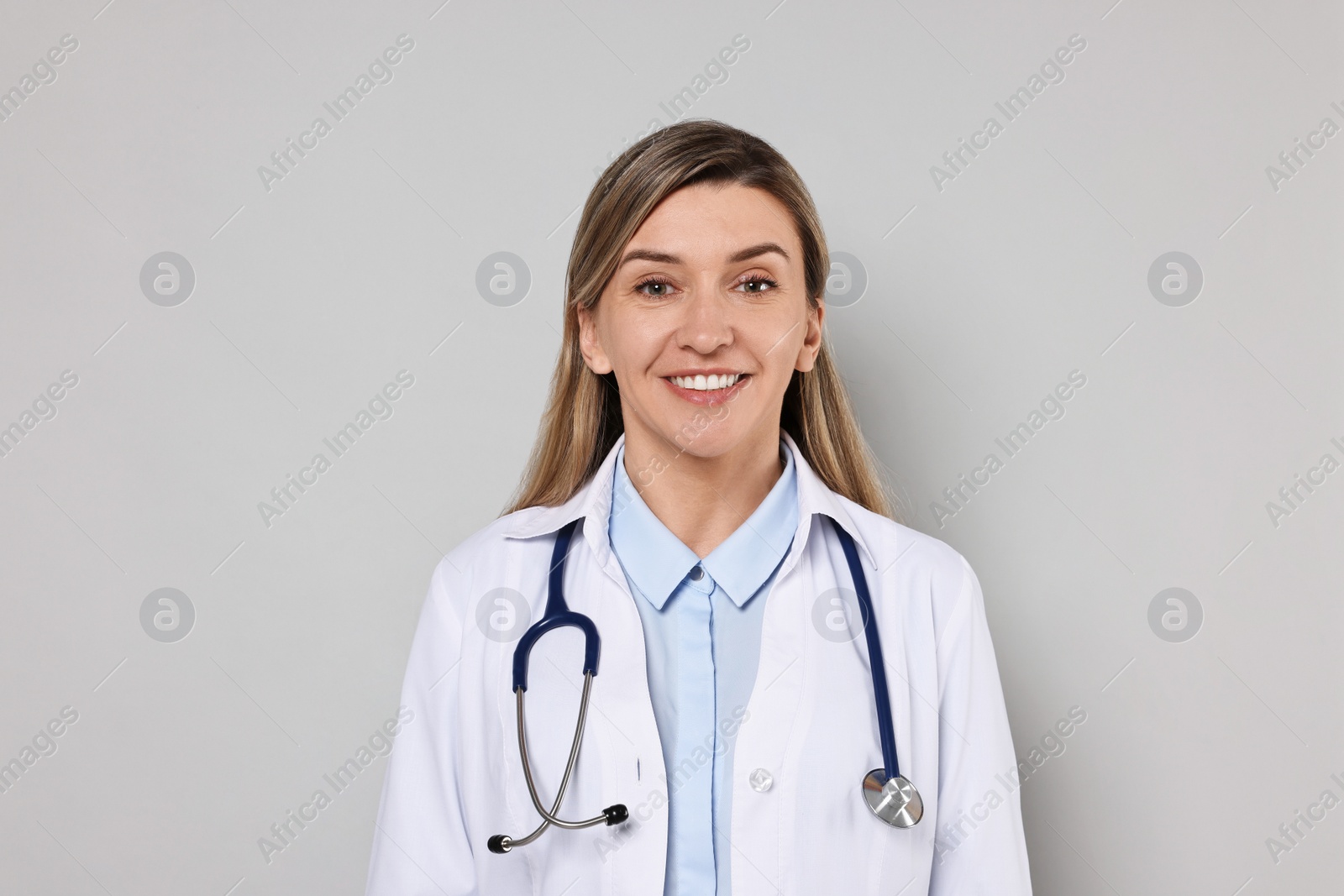 Photo of Portrait of happy doctor with stethoscope on light grey background