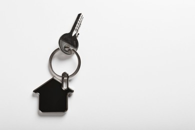 Photo of Key with trinket in shape of house on white background, top view and space for text. Real estate agent services