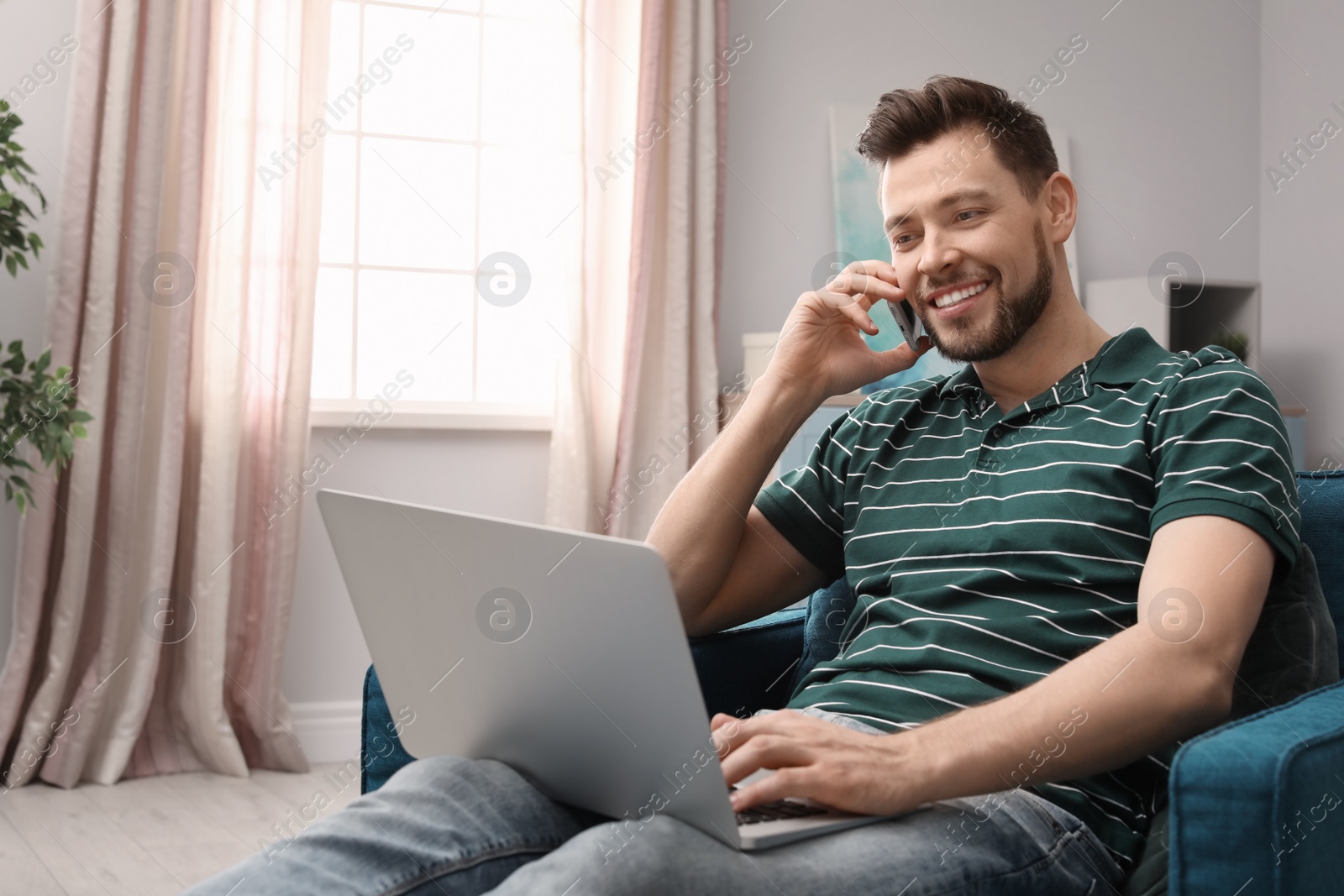 Photo of Young man working with laptop on armchair in home office