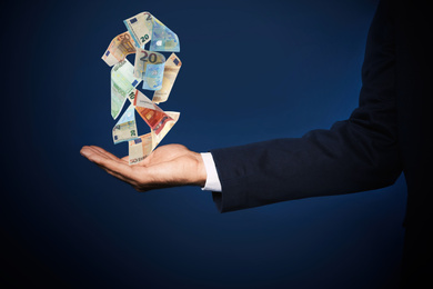 Businessman with money on dark blue background, closeup. Currency exchange