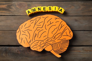 Yellow cubes with word Amnesia and paper cutout of human brain on wooden table, top view