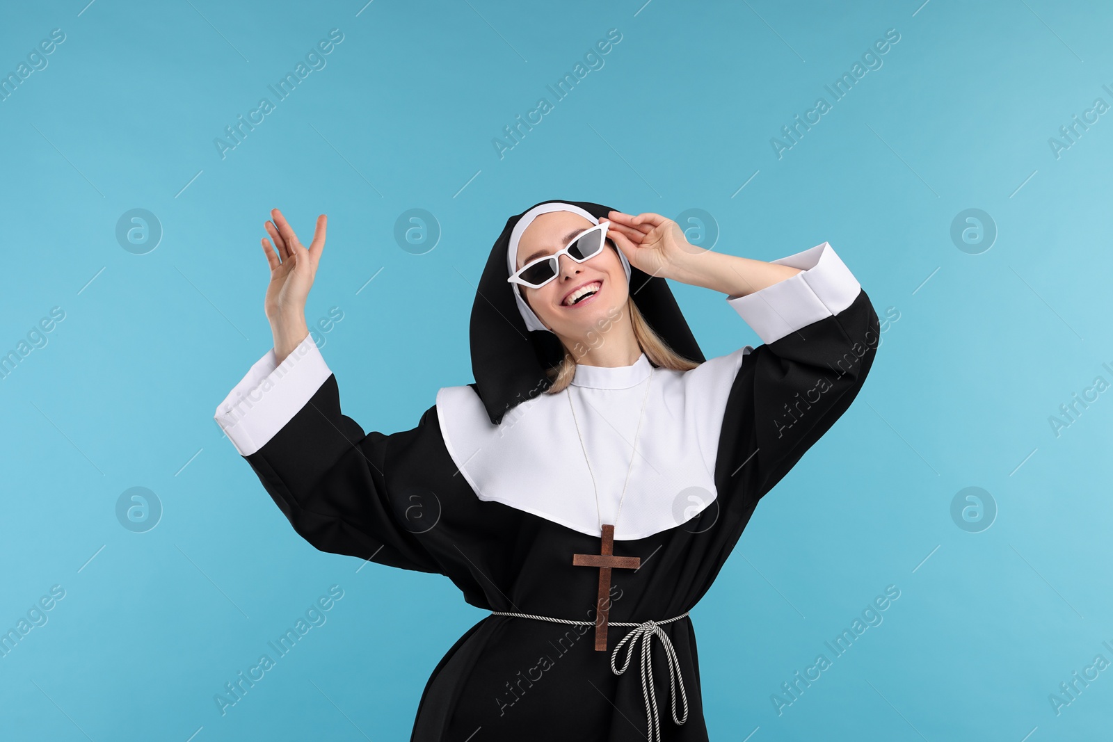 Photo of Happy woman in nun habit and sunglasses against light blue background