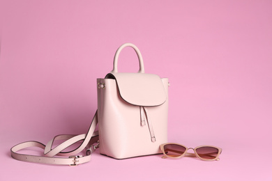 Photo of Stylish woman's backpack and sunglasses on light pink background