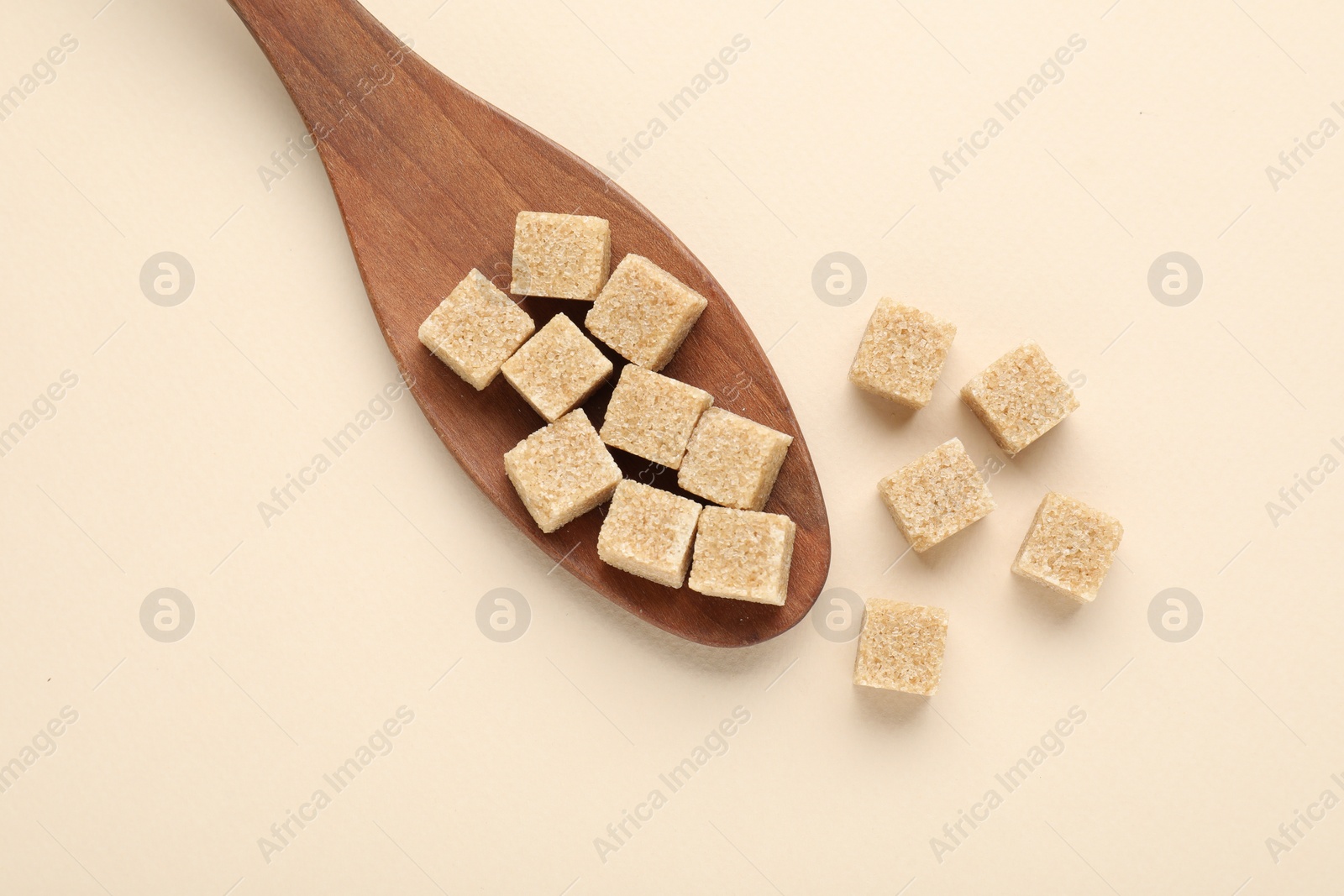 Photo of Brown sugar cubes and wooden spoon on beige background, top view