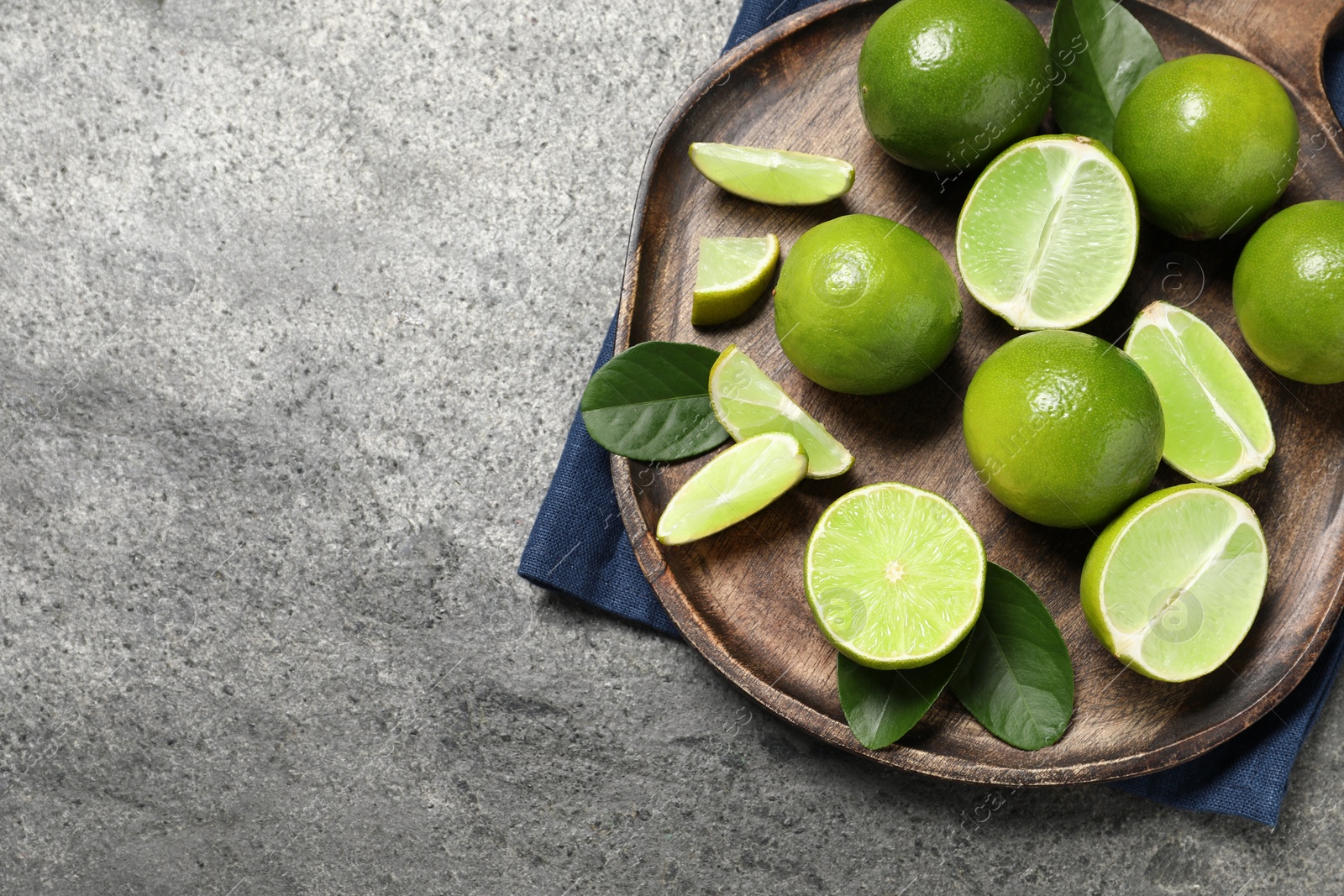 Photo of Fresh ripe limes and leaves on grey table, top view. Space for text