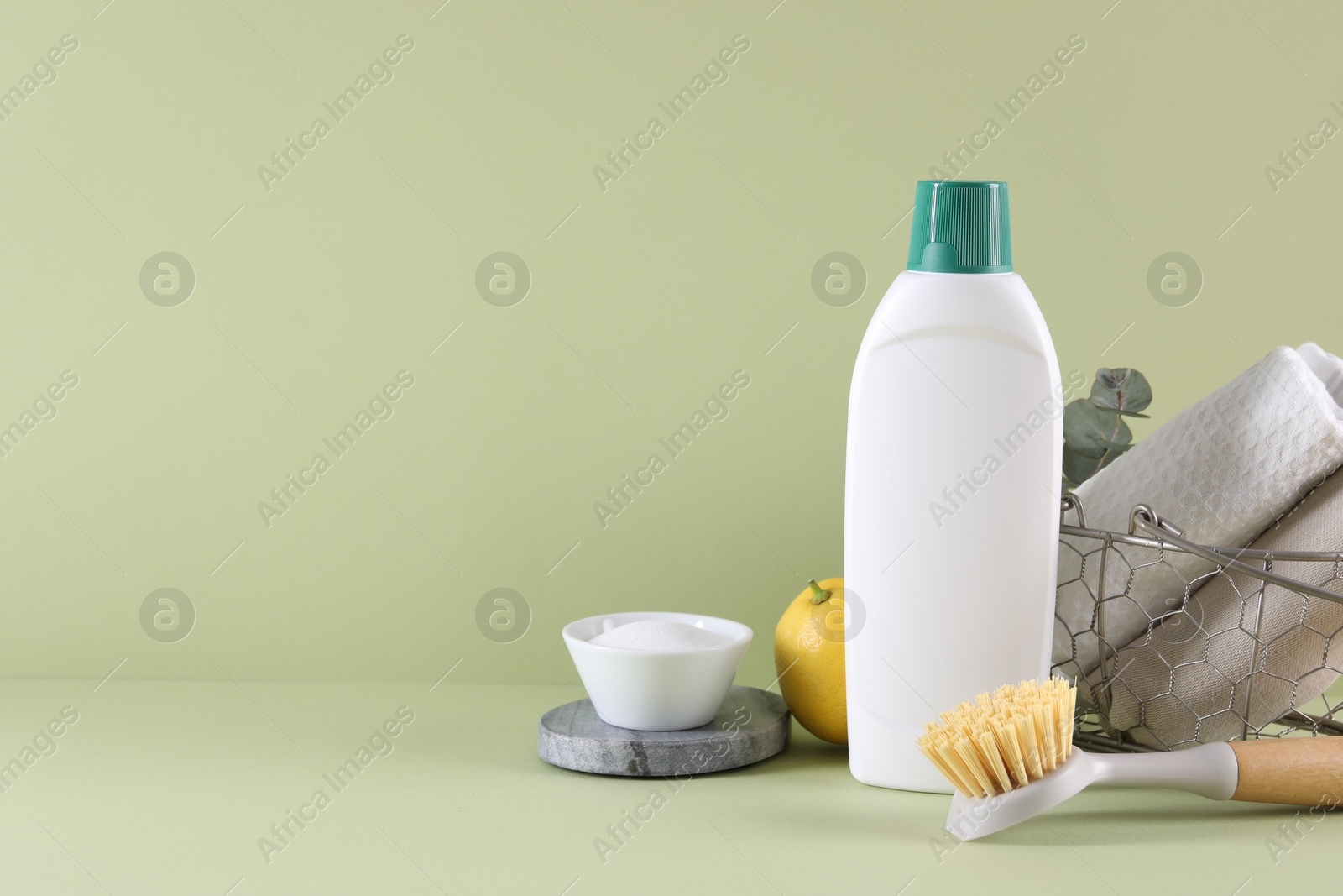 Photo of Bottle of cleaning product, baking soda, lemon and brush on light green background. Space for text