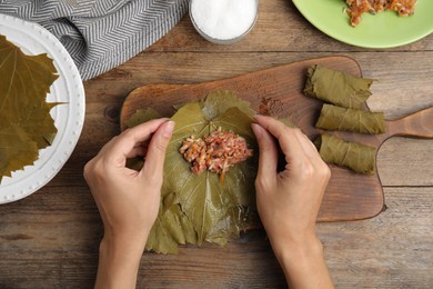 Photo of Top view of woman preparing stuffed grape leaves at wooden table, closeup